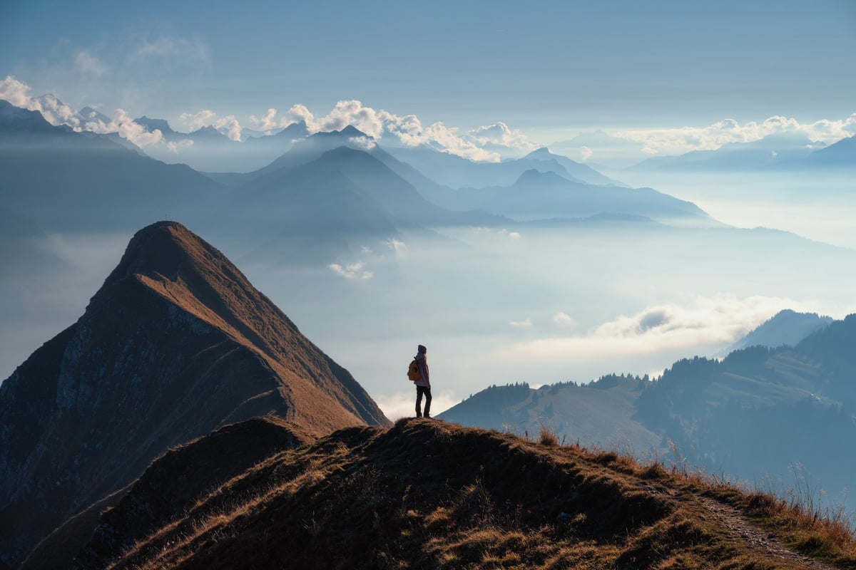 Person overlooking a mountain ridge at sunset, representing a moment of quiet reflection about the future